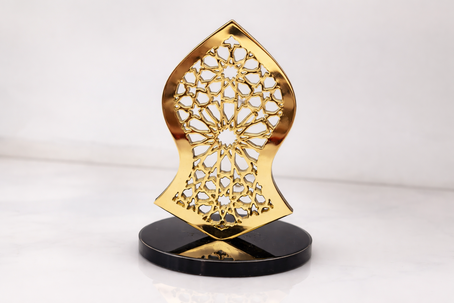 Decorative gold object with intricate design on a black stand against a white background