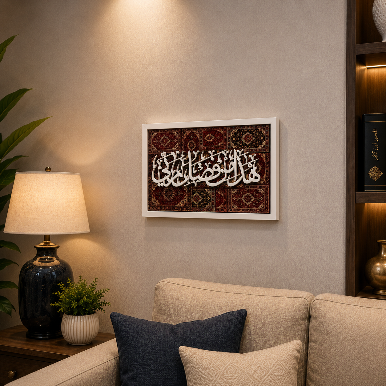 A framed Islamic wall art piece featuring white Arabic calligraphy over a red and brown patterned rug design, displayed on a beige wall above a sofa in a styled living room setting.