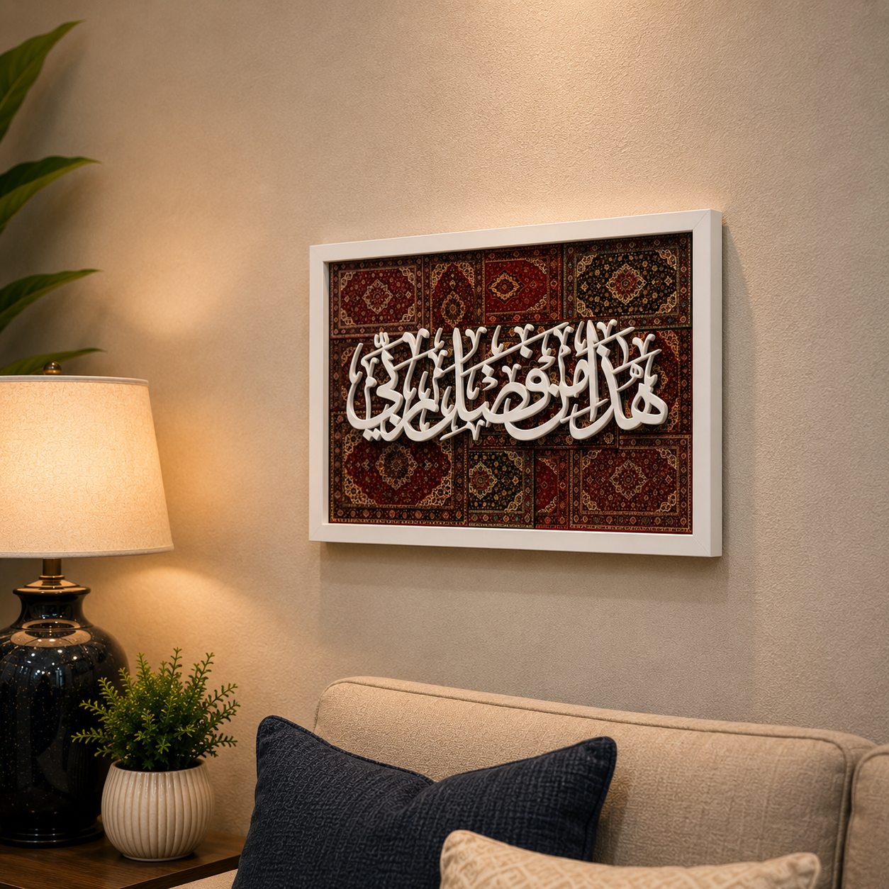 Framed Islamic wall art featuring white Arabic calligraphy over a red and brown patterned rug design, displayed on a beige wall above a sofa in a styled living room setting.