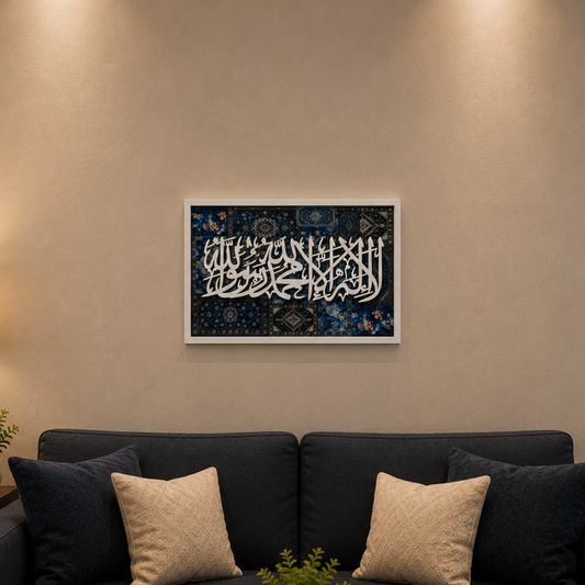 A framed piece of Arabic calligraphy wall art with a dark blue and black background and white script, displayed in a modern living room setting above a dark blue sofa with beige throw pillows.