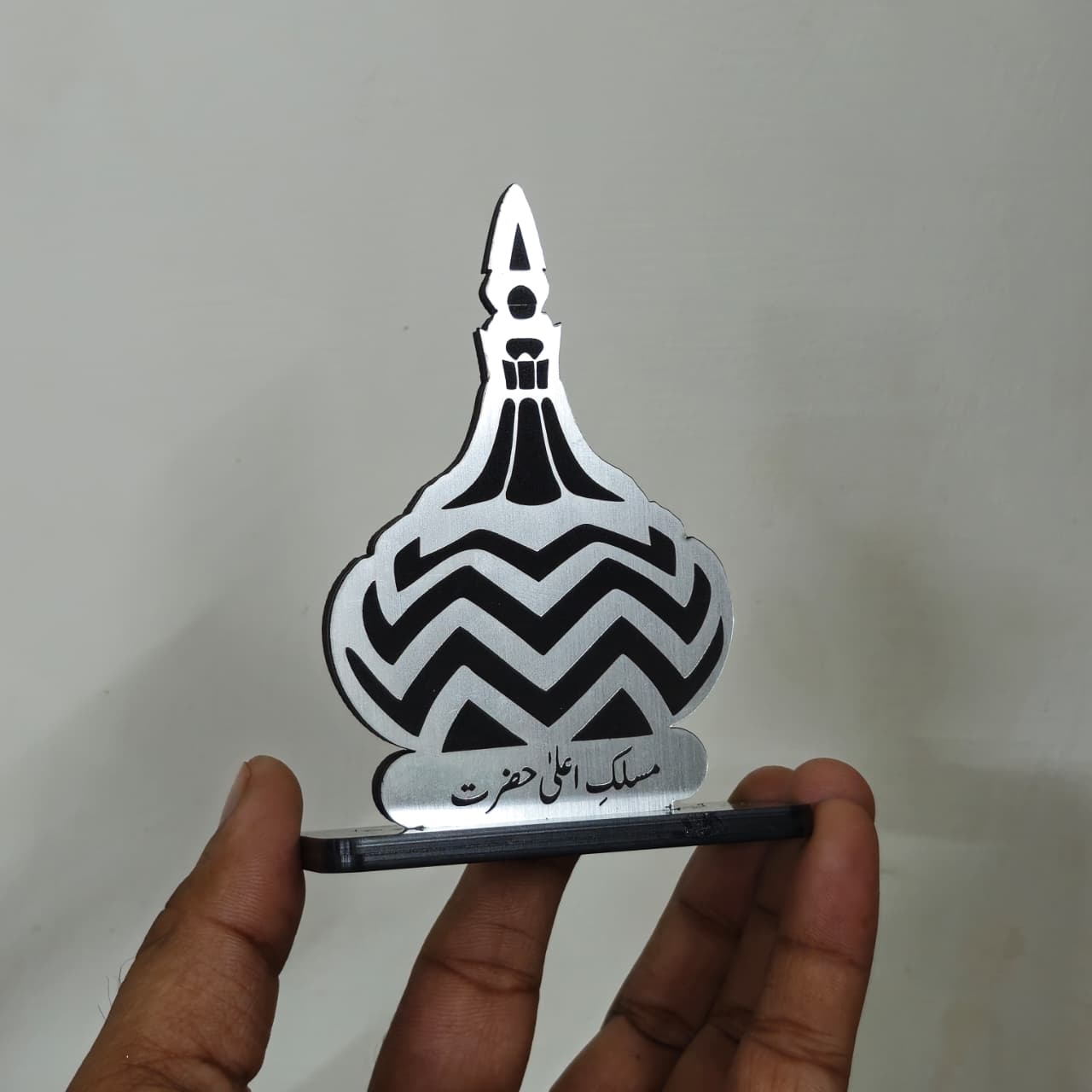 Metallic object with black zigzag pattern held by a hand against a plain background
