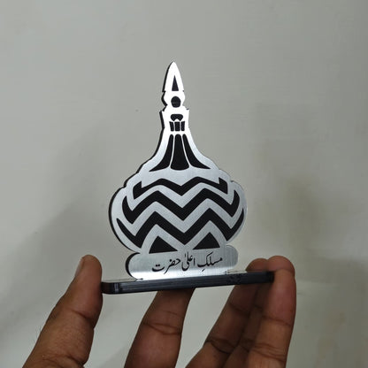 Metallic object with black zigzag pattern held by a hand against a plain background