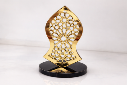Decorative gold object with intricate design on a black stand against a white background