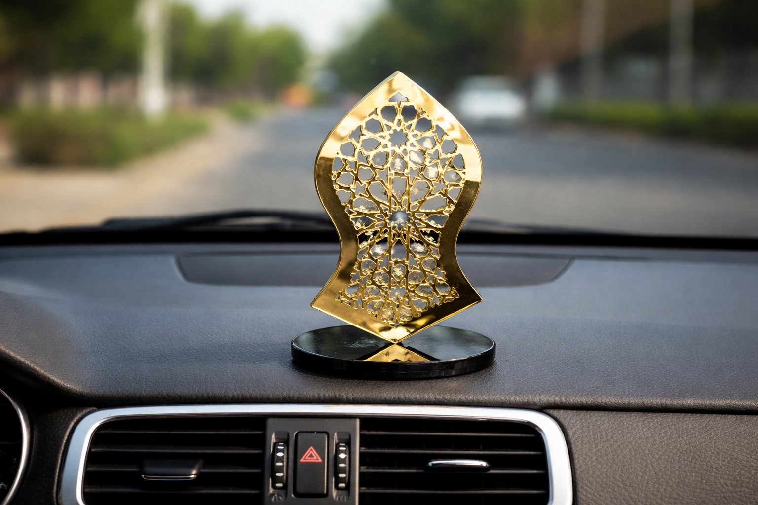 Decorative gold car air freshener on a car dashboard with a blurred road background