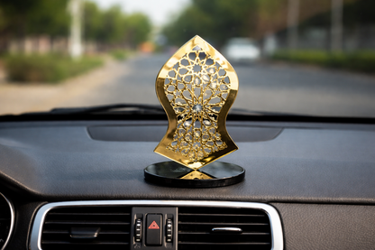 Decorative gold car air freshener on a car dashboard with a blurred road background