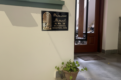 Entrance to a building with a nameplate and a potted plant on a concrete floor.