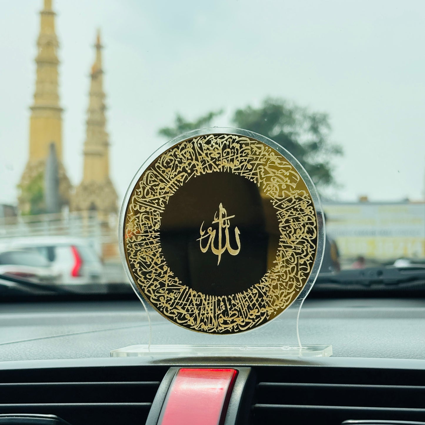 Decorative car air freshener with gold and black design on a car dashboard, with blurred background of a building.