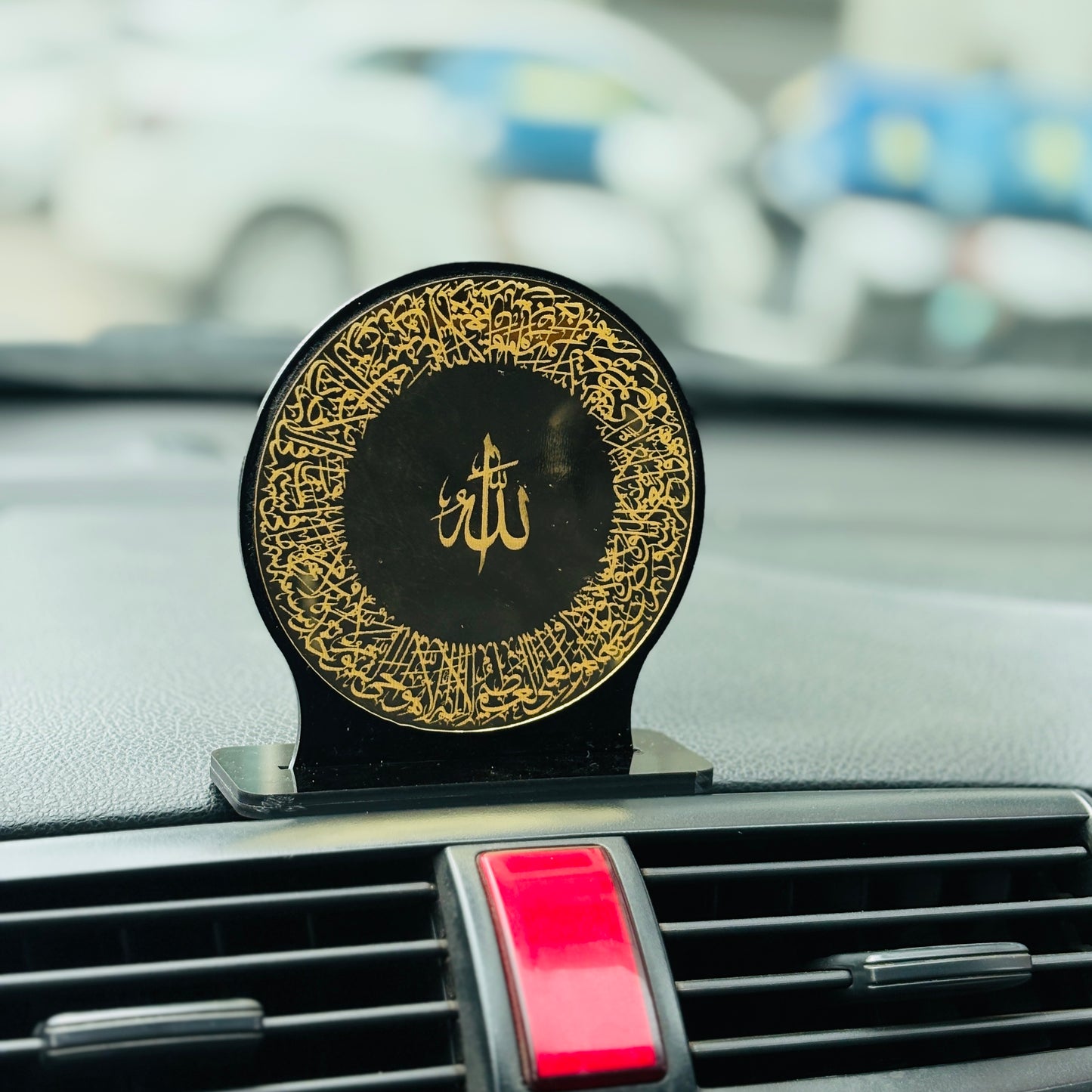 Decorative car dashboard accessory with gold patterns and 'Allah' symbol on a black background.