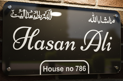 Black nameplate with white text displaying 'Hasan Ali' and 'House no 786' against a brick wall background.