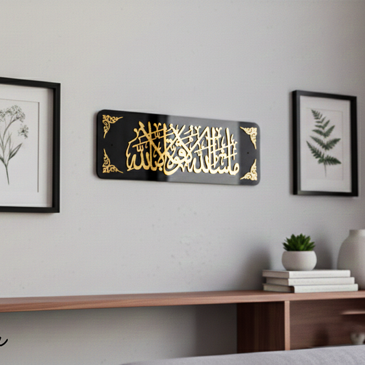 Decorative wall art with gold calligraphy on a black background, displayed on a wall above a wooden shelf.