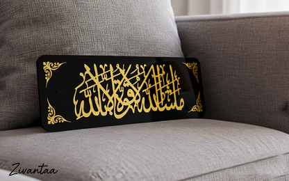 Decorative black plaque with gold Arabic calligraphy on a gray couch